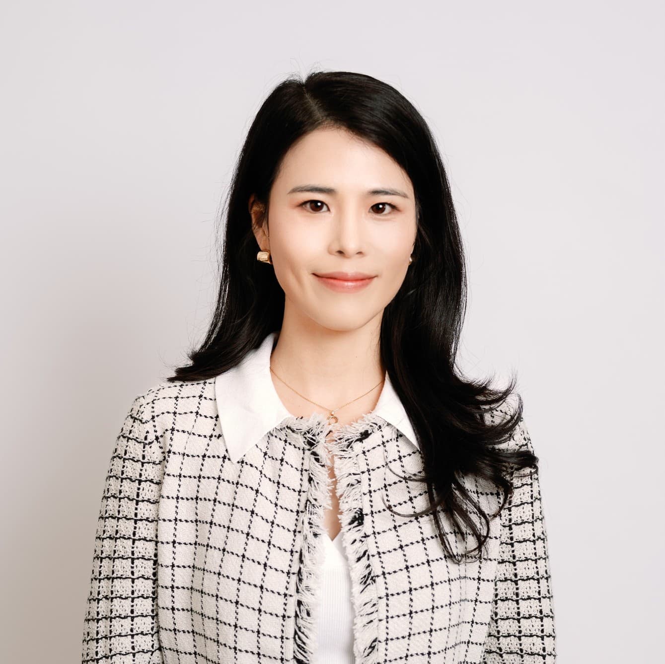 Smiling woman with long black hair wearing a white and black checkered tweed jacket.